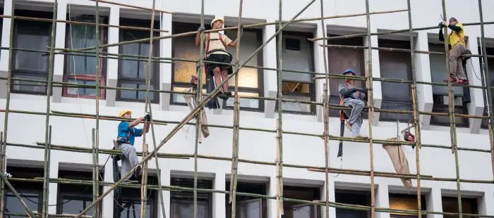Stavební dělníci pracují na lešení u okenních otvorů.