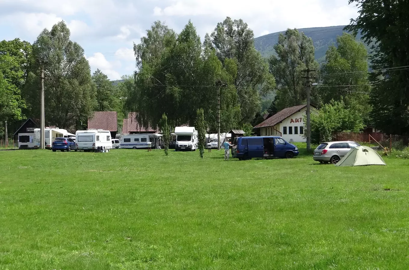 Autokemp v Hejnicích s karavany, vozy a stanem na trávníku.