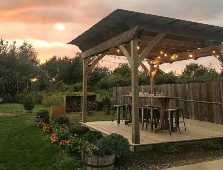 Dřevěná pergola s trámy na zahradě při západu slunce.