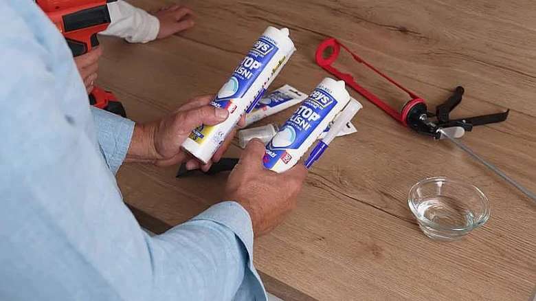 Dvě tuby silikonu s pistolkou na stolu pro aplikaci kolem vany.