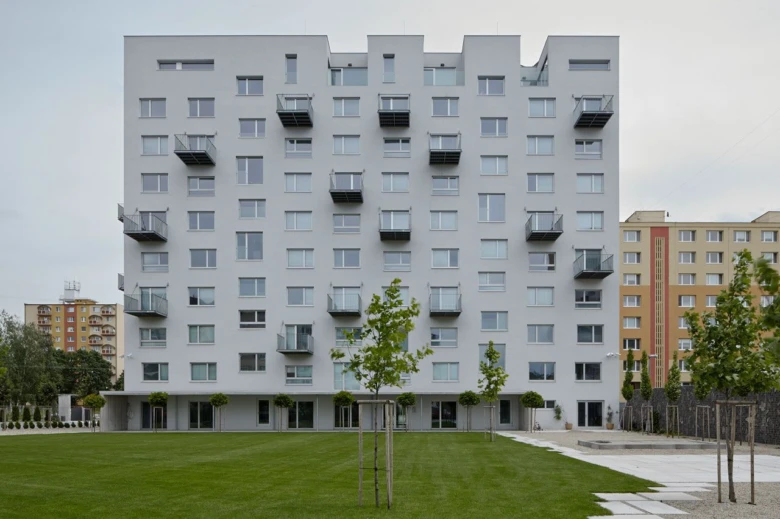 Moderní bílá panelová budova s balkóny na zelené trávníku.