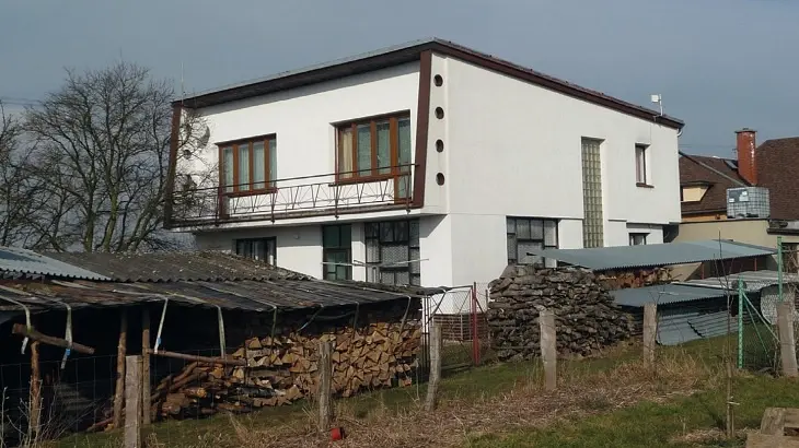 Moderní bílý dům s dřevěným ohništěm v pozadí.