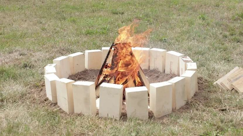 Ohniště postavené z cihel s hořícím ohněm na trávníku.