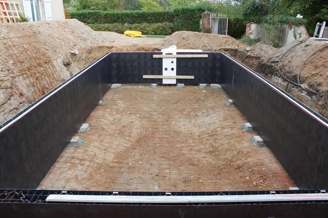Stavba bazénu: vykopaný jáma s černou hydroizolací a příprava na betonování.