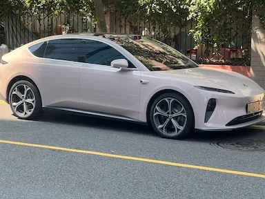 Bílé elektromobil zaparkovaný na ulici s dřevěným plotem.