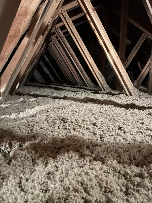 Loose stone wool insulation installed in a wooden attic roof structure.