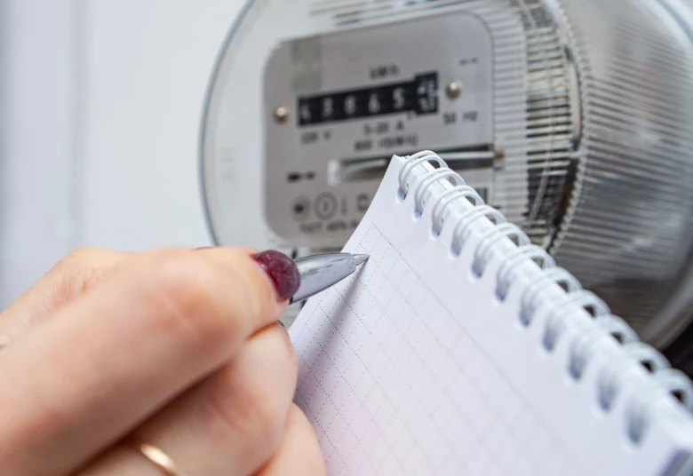 Ruka zapisuje čísla z elektroměru do sešitu.
