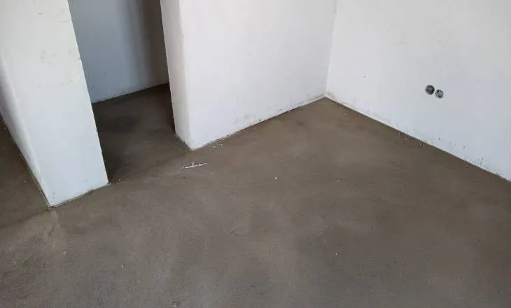 Nedokončená betonová podlaha v prázdné místnosti s bílými stěnami.