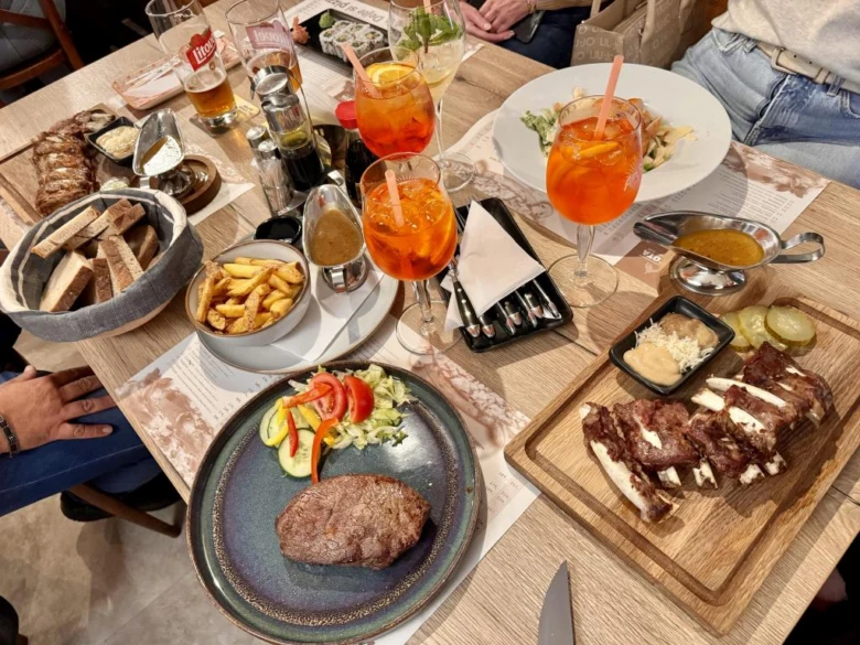 Stůl plný jídla v restauraci s masem, salátem a nápoji.