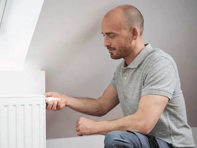 Muž nastavuje termostat na bílém radiátoru v interiéru.