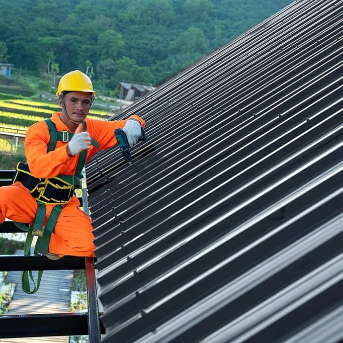 Montáž trapézových plechů na střechu pracovníkem s elektrickým nástrojem.