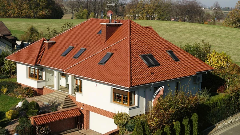 Moderní dům s červenou sedlovou střechou na pozadí zelených polí.