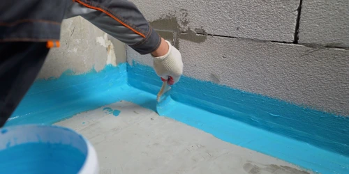 Pracovník nanáší modrou hydroizolační směs na betonovou stěnu.