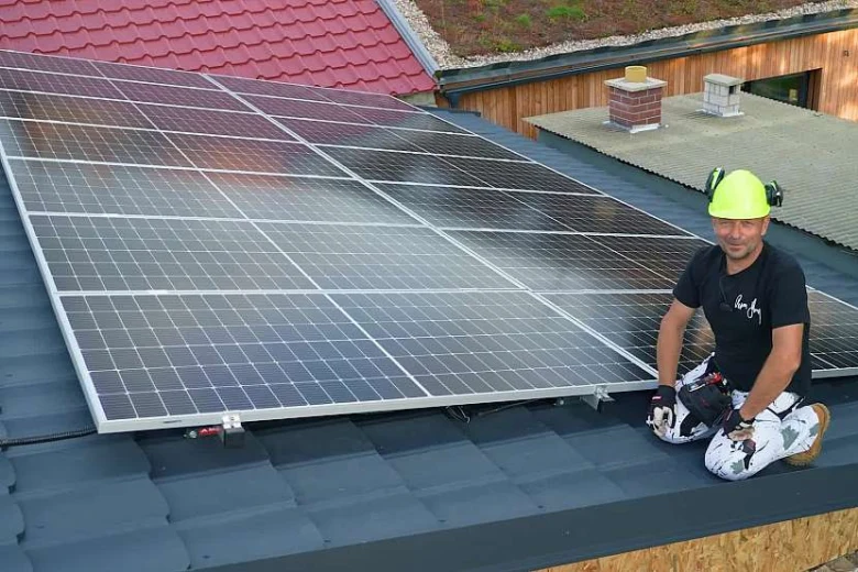 Muž montuje fotovoltaický panel na střechu domu.