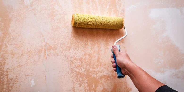 Ruka s válečkem nanáší barvu na přípravenou stěnu před malováním.