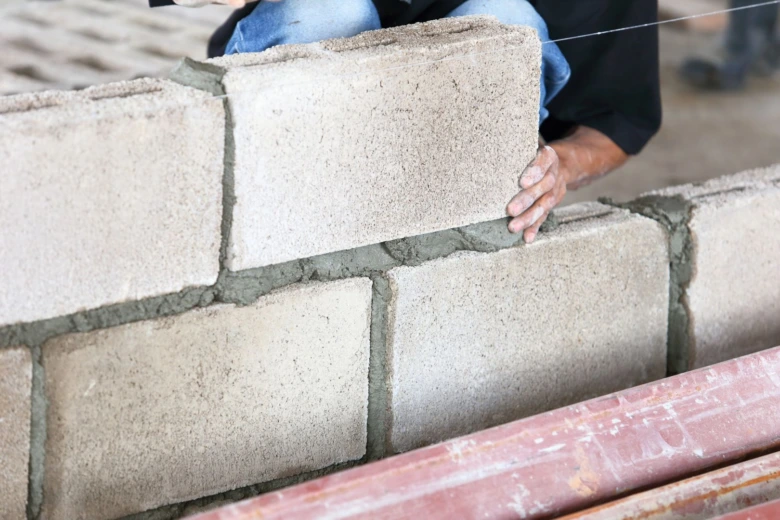 Stavebník kladí betonové tvary do zdi s maltou.
