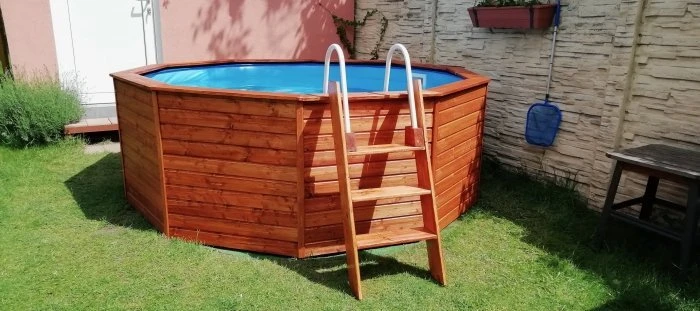 Dřevěný nadzemní bazén s dřevěným obložením na trávníku.