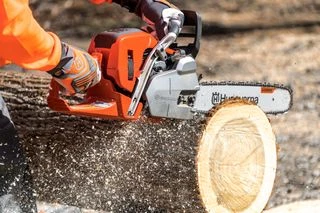 Oranžová motorová pila řezí dřevo s výstřikem pilin.