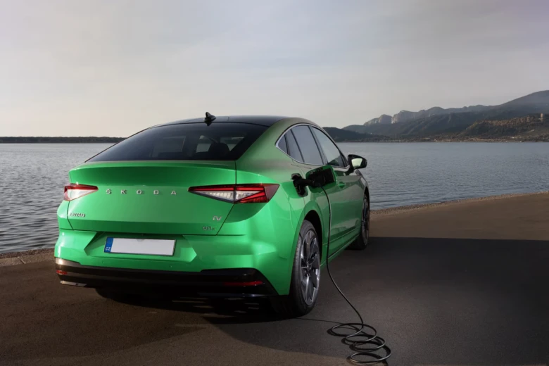 Zelené elektromobilové auto nabíjené u jezera s horami na pozadí.