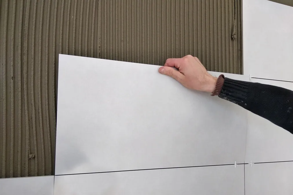 Ruční montáž velkoformátové dlažby na stěnu s lepidlem.