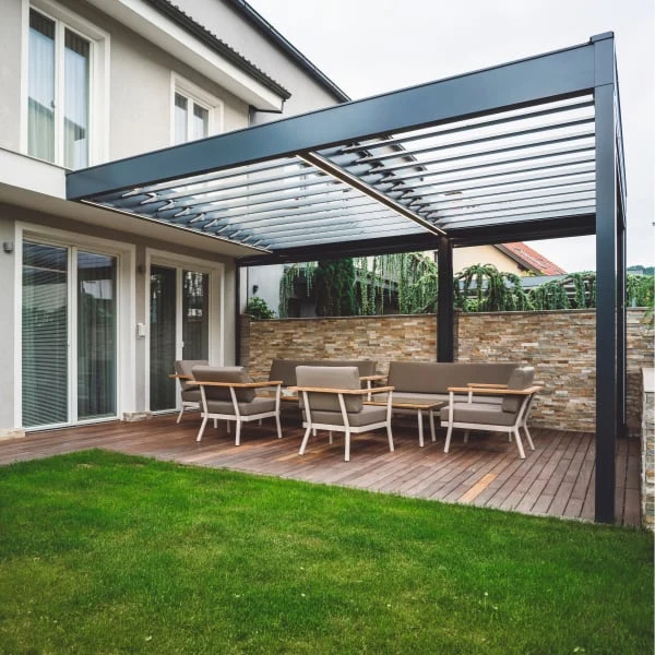 Moderní kovová pergola na dřevěné terase u domu s venkovním nábytkem.