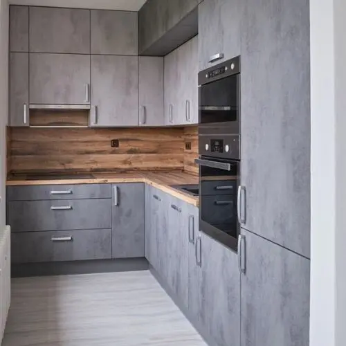Moderní kuchyň po rekonstrukci s šedými skříněmi a dřevěnou podlahou.