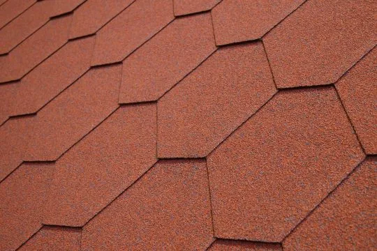 Červené asfaltové šindele na střeše jako stavební materiál.