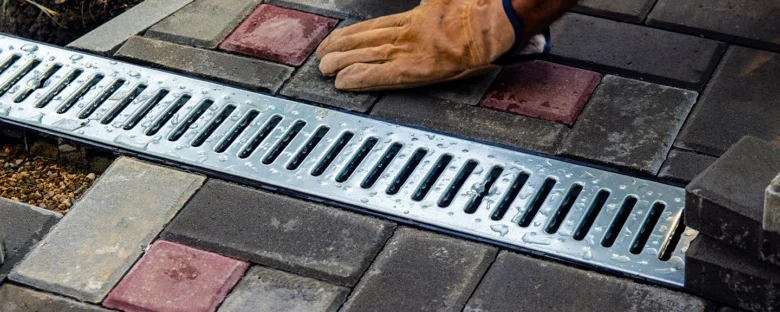 Instalace kovového odvodňovacího žlabu do dlažby zahrady s rukavicí.