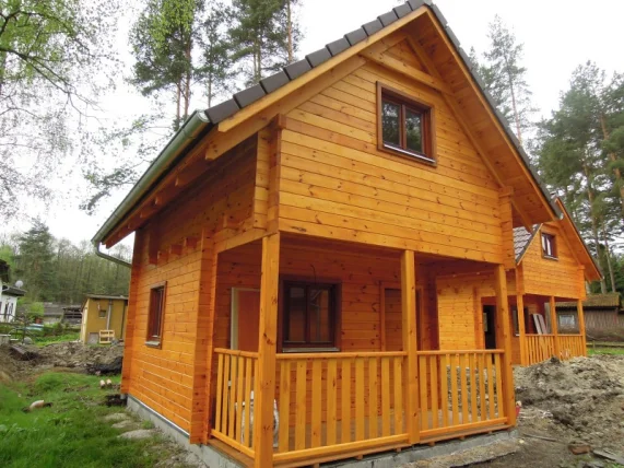 Dřevěná chata s podkrovím a další malé dřevostavby v lese.