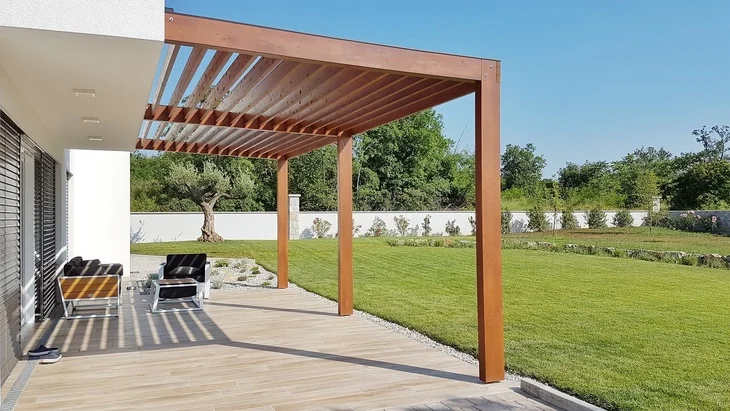 Moderní dřevěná pergola připojená k domu s venkovním posezením.