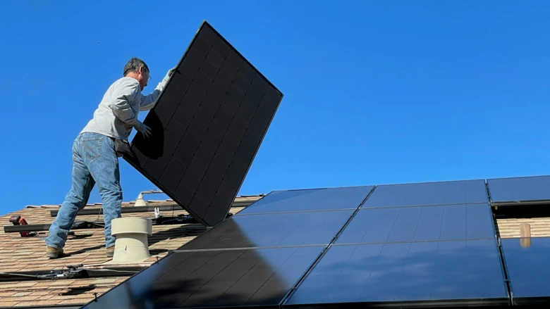 Muž montuje solární panel na střechu domu.