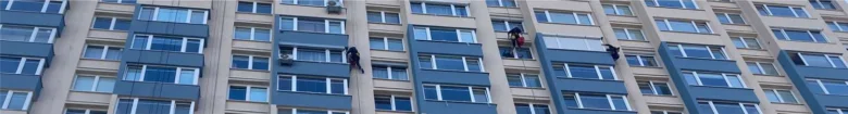 Pracovníci umývají okna na fasádě bytového domu.