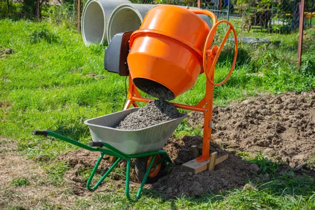 Oranžový betonovač nalévá směs do vozíku na staveništi.