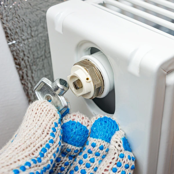 Ruka s rukavicí odvzdušňuje radiátor pomocí klíčového ventilu.