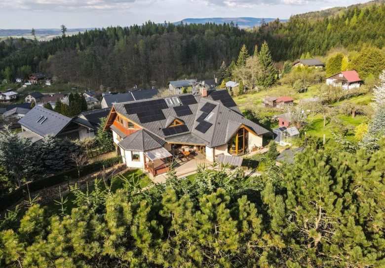 Rodinný dům s fotovoltaickými panely na střeše v lesním prostředí.
