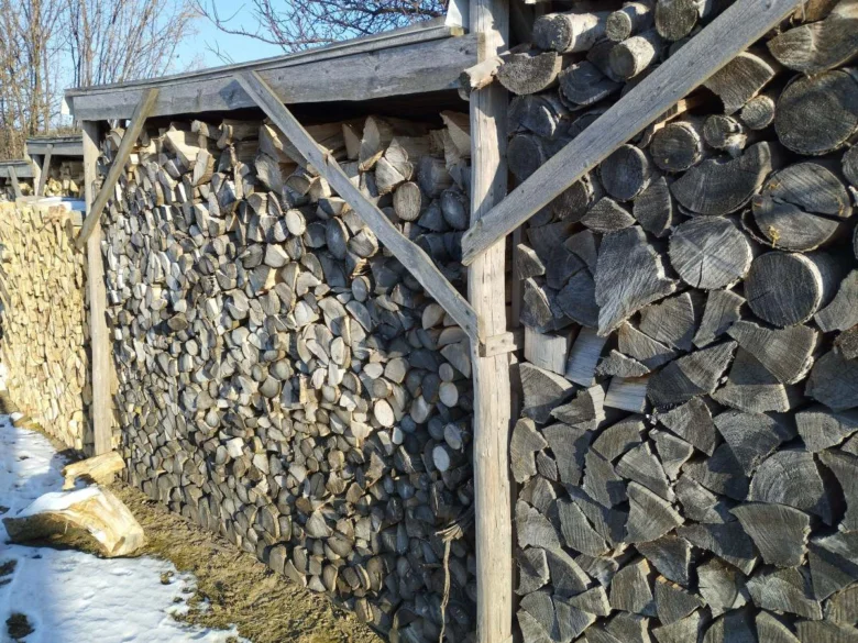 Dřevník s přístřeškem plný naskládaného dříví venku.