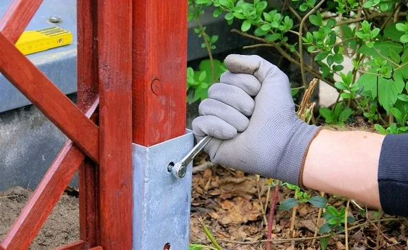 Ruka utahuje šroub kovové podložky na dřevěný sloup.