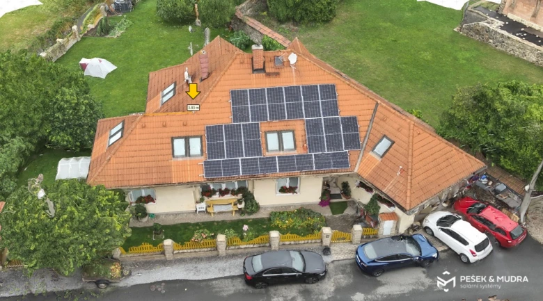 Rodinný dům s fotovoltaickými panely na střeše a parkujícími auty.