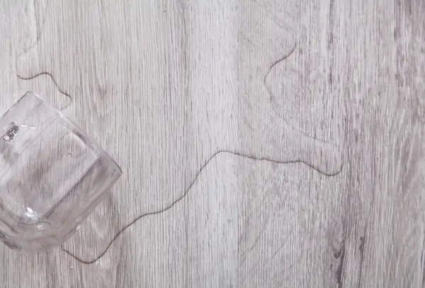 Voda z hrnku rozlitá na vinylové podlaze s dřevotiskem.