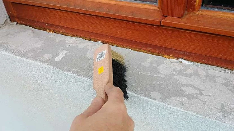 Ruka čistí betonový parapet před montáží vnitřního okenního prahu.