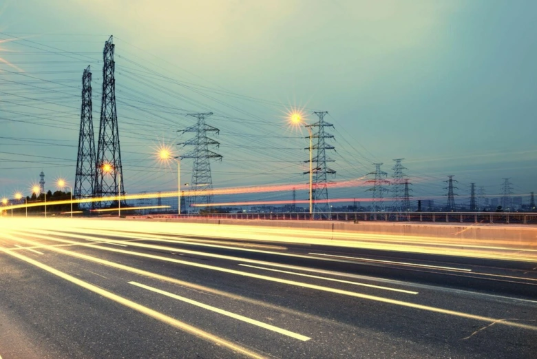 Dálnice s výraznými stopy světel vozidel pod elektrickými vedeními v noci.