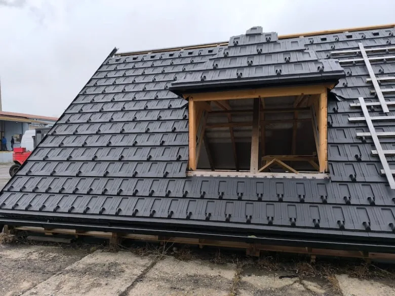 Instalace tmavých plastových střešní tašek na dům s oknem.