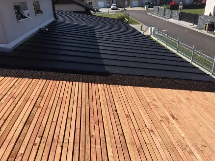Moderní střecha s tmavými taškami vedle dřevěné terasy.