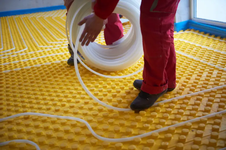 Instalace podlahového topení s rozvodem potrubí na žluté desce.