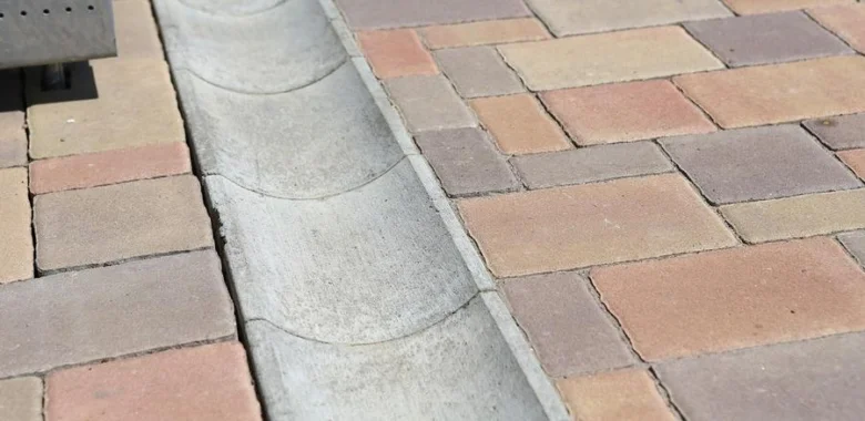 Konkrétní drenážní žlábek mezi dlažbou u domu.