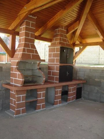Venkovní kuchyň s kamny pod dřevěnou střechou altánu.