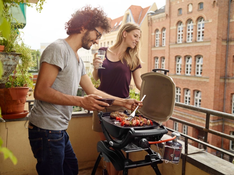 Muž a žena grilují na plynovém grilu na balkóně.