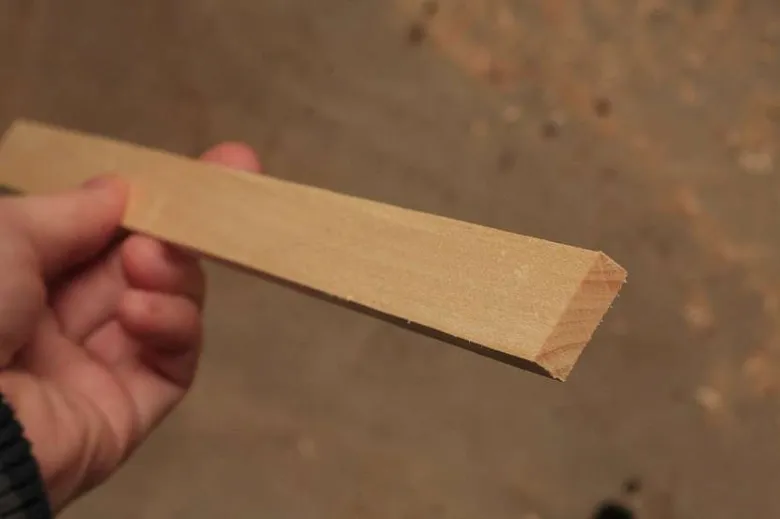 Ruka drží dřevěný omítník s zaobleným koncem.