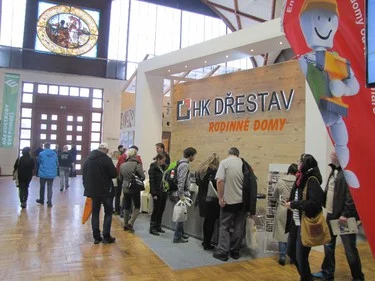 Stánek dřevostavební firmy na výstavě s lidmi prohlížejícími materiály.