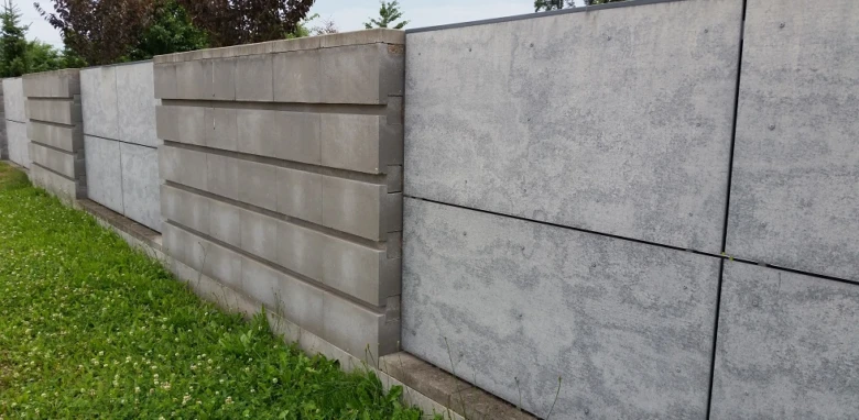 Řada betonových plotů z prefabrikovaných desek na trávníku.